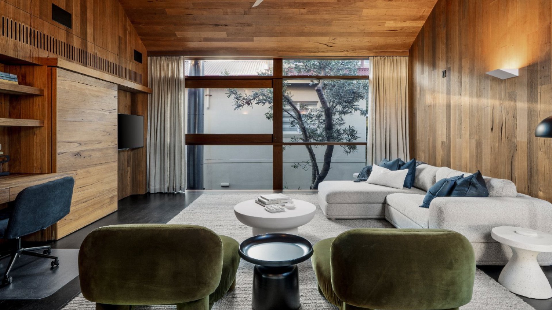 Timber-lined living room with green velvet armchairs and an outlook to the garden
