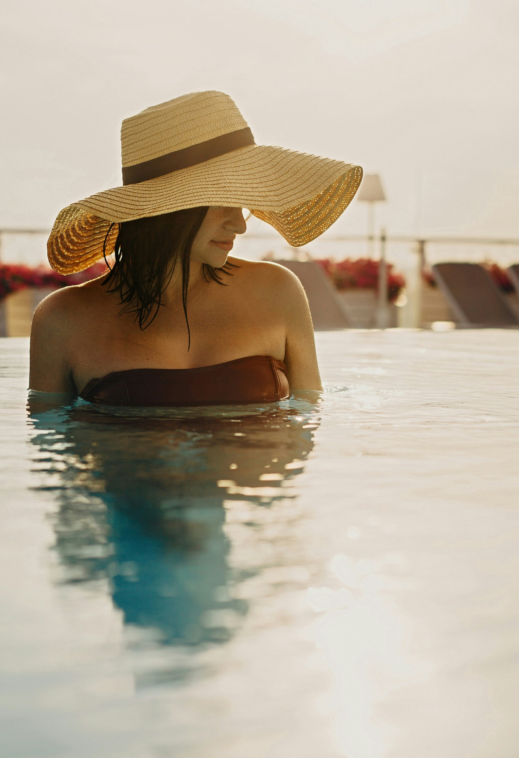 Woman in a wide-brimmed straw hat standing in a rooftop pool