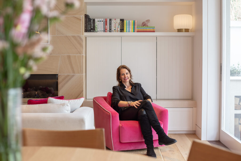 Amy in the pink armchair beside the sandstone fireplace and bookshelves