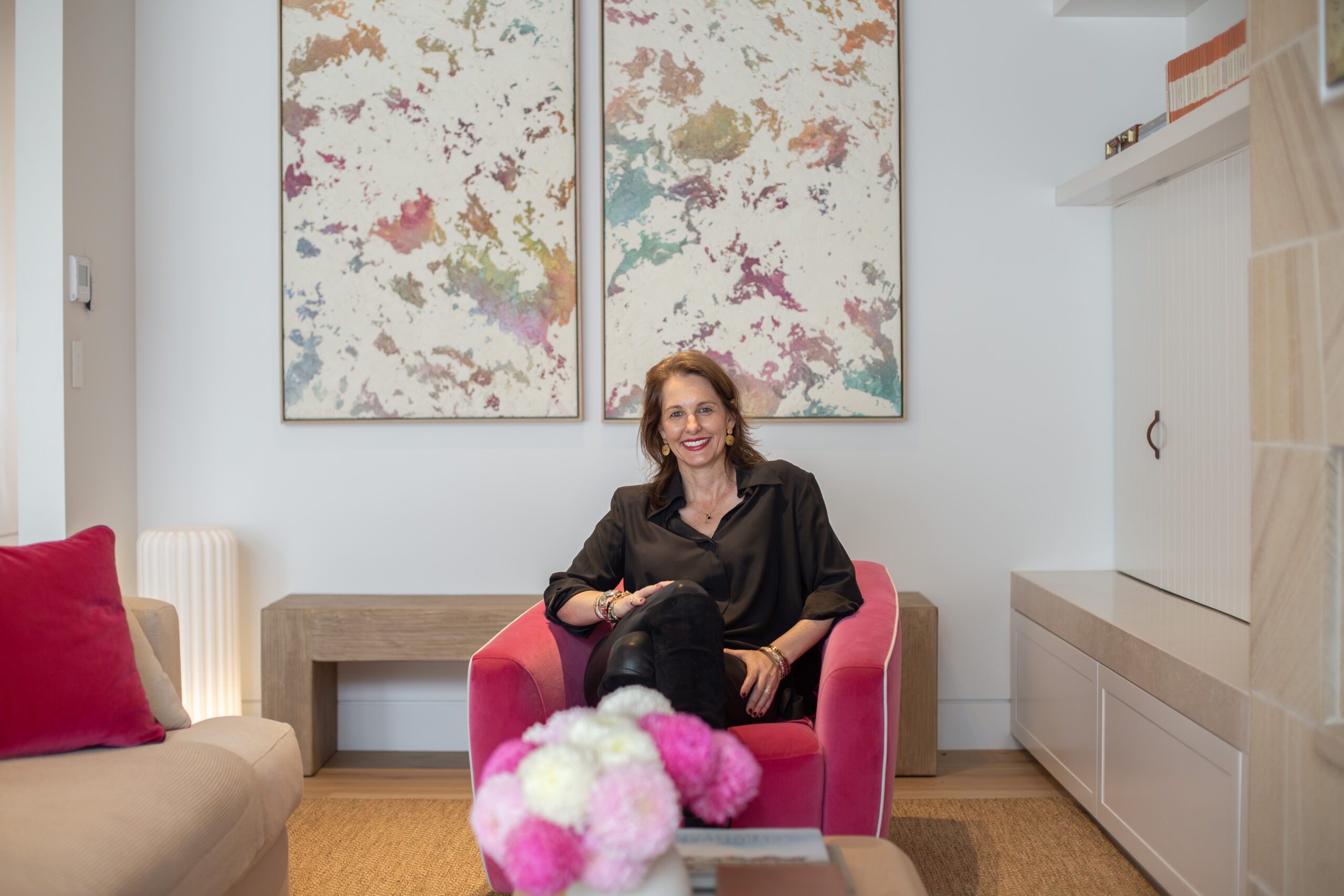 Amy, the owner of Spicer Street Cottage, seated in a pink velvet armchair beneath two abstract paintings