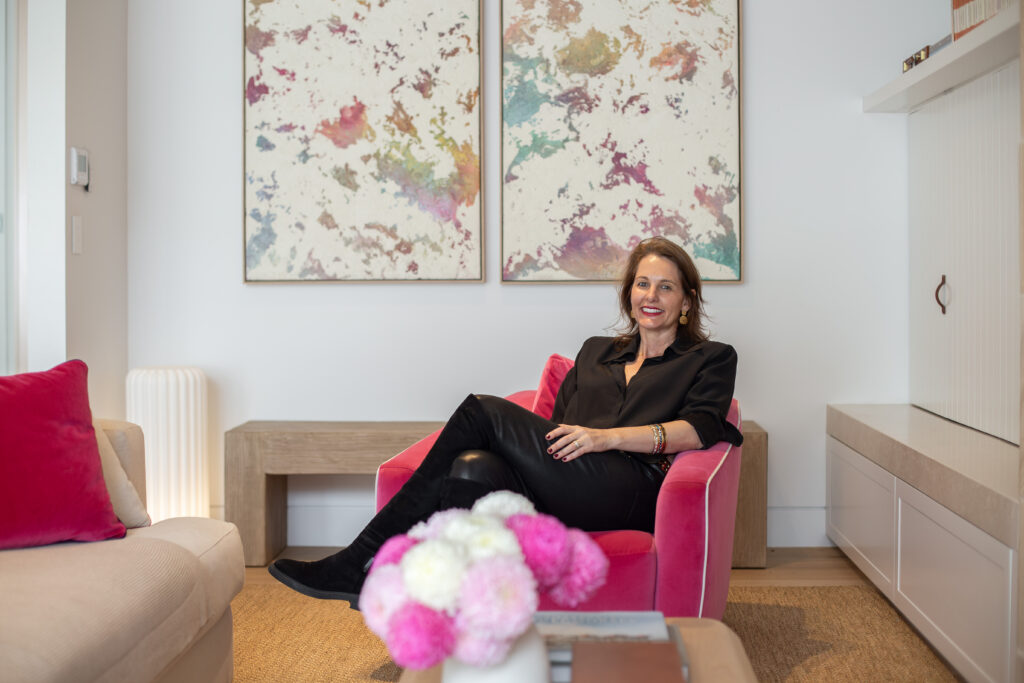Amy relaxing in a pink velvet armchair beneath two abstract paintings