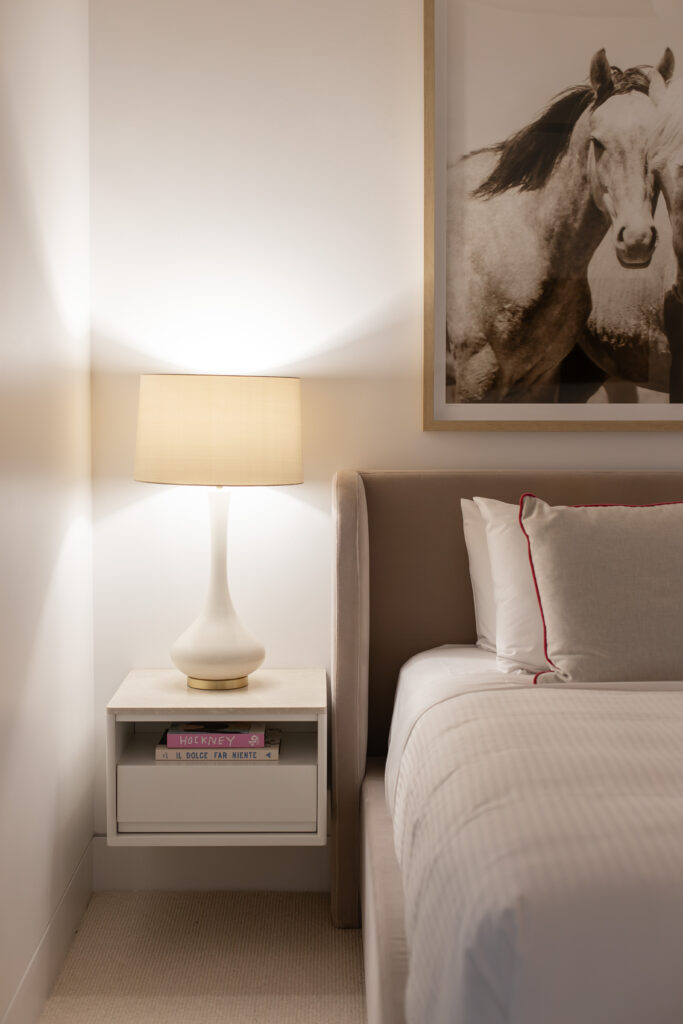 Bedside lamp and upholstered bedhead beneath a framed photograph of horses