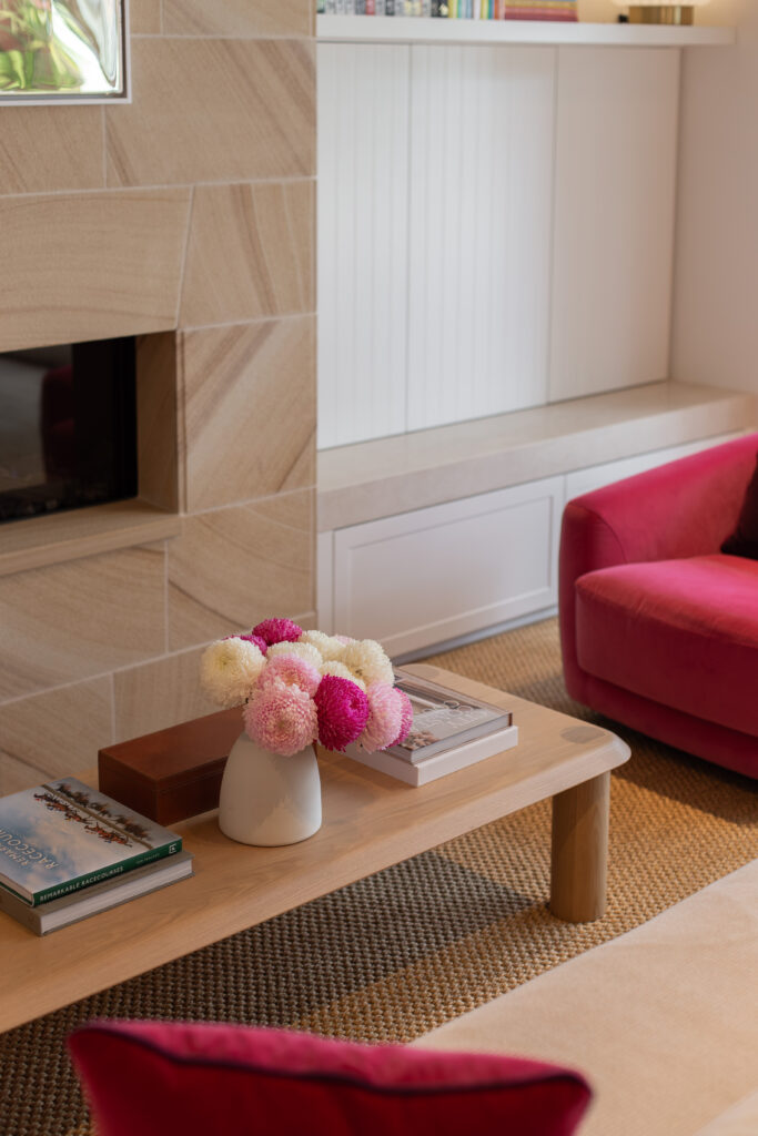 Flowers on the coffee table beside the sandstone fireplace and a pink armchair