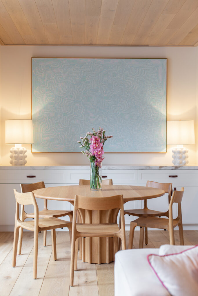 Round oak dining table and chairs beneath a large pale blue painting