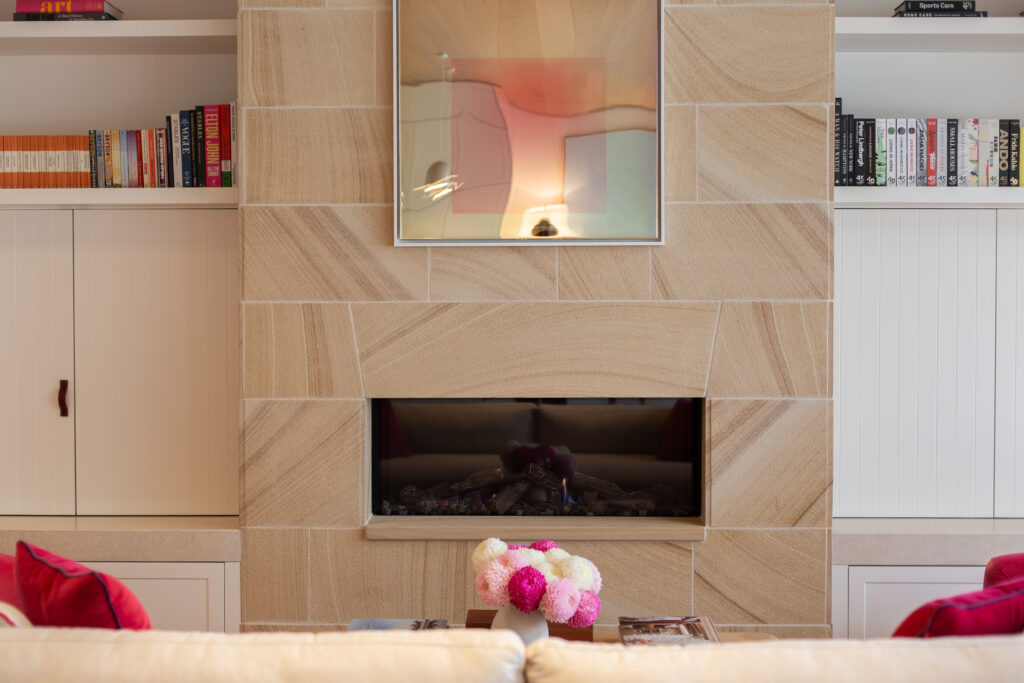 Sandstone fireplace with an artwork hung above it, between white bookshelves
